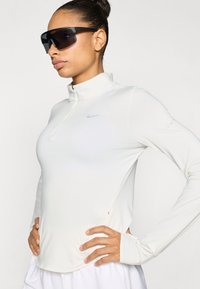 Άσπρο αθλητικό μπλουζάκι μακρυμάνικο με ψηλό γιακά, φερμουάρ μέχρι το ένα τέταρτο και διακριτικό λογότυπο Nike. Ομαλό ύφασμα και εφαρμοστό σχέδιο που βελτιώνουν την κινητικότητα.