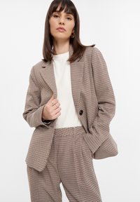 Karierter Blazer in Braun- und Cremetönen mit lockerer Passform, Reverskragen und großen Knöpfen, kombiniert mit passenden Hosen. Glatte Stofftextur.