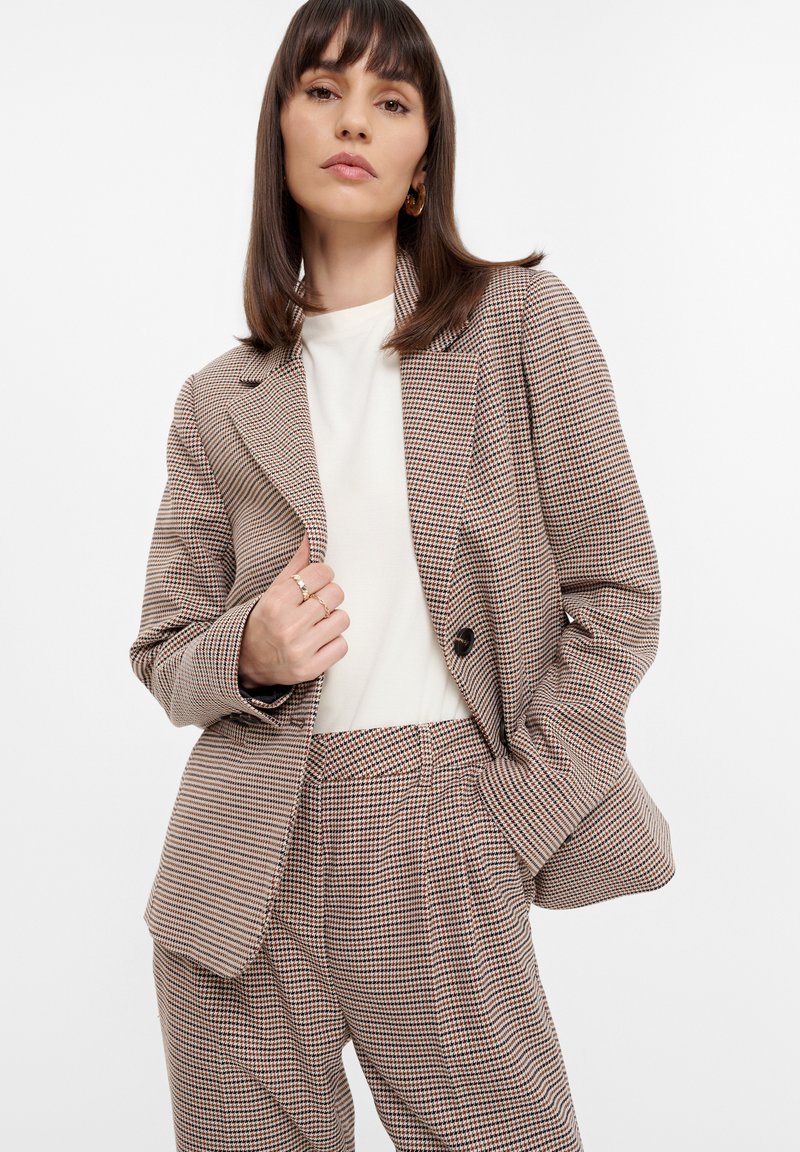 Karierter Blazer in Braun- und Cremetönen mit lockerer Passform, Reverskragen und großen Knöpfen, kombiniert mit passenden Hosen. Glatte Stofftextur.