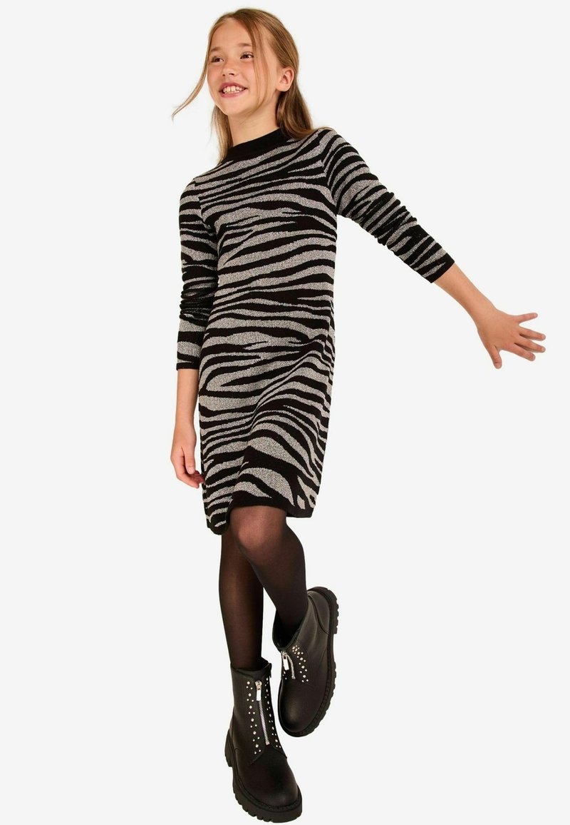 Schwarz und silber gestreiftes Strickkleid mit langen Ärmeln, kombiniert mit schwarzen Knöchelstiefeln mit silbernen Nieten und einem Reißverschluss.
