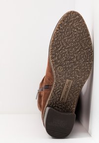 Semelle d'une botte en daim marron avec une semelle antidérapante texturée, taille 37, et étiquette de marque "Tamaris" visible sur le côté extérieur.
