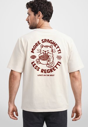 Mann trägt ein weißes T-Shirt mit rotem Aufdruck einer Katze, die Spaghetti isst, und dem Text „Mehr Spaghetti, weniger Reue“ auf dem Rücken.