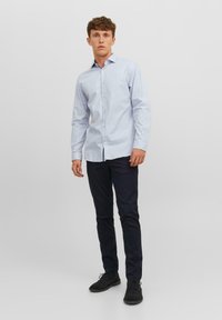 Cămașă albastră deschis cu mânecă lungă, cu un model subtil, guler tip button-down și nasturi, combinată cu pantaloni închisa și pantofi negri.