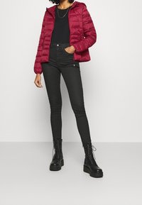 Burgunderfarvet dunjakke med hætte, sort tætsiddende top og højtsiddende sorte skinny jeans, kombineret med sorte chunky snørestøvler.