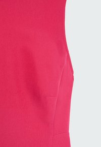 Gros plan d’un vêtement rouge sans manches montrant un tissu lisse et des détails de couture ajustés sur le côté.