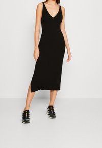 Svart ribbad midiklänning med djup V-ringning, med slitsar i fållen, kombinerad med svarta sneakers för sportigt utseende.