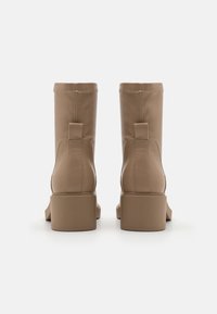 Bottines en cuir beige avec une texture lisse, bout carré et talon carré. Elles sont dotées de deux poignées à l'arrière pour un enfilage facile.