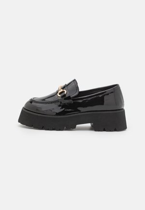 Mocassins en cuir verni noir avec une semelle épaisse noire, des accessoires en or et une finition lisse et brillante. Possède un design à bout arrondi.