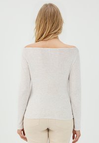 Lichtbeige langemouwtop met een off-the-shoulder ontwerp, gemaakt van zacht, geweven stof. Heeft een rechte zoom. Zichtbare stiksels.