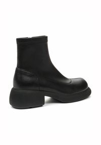 Botas de cuero negro hasta el tobillo con un acabado suave, punta redonda y tacón de goma grueso. Presenta costuras sutiles a lo largo del borde superior.