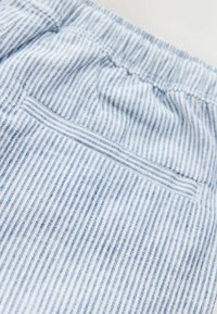 Detailný záber na modro-bielo pruhovanú látku s elastickým pásom a horizontálnym zadným vreckom na odeve.