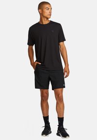 Schwarzes T-Shirt mit kurzen Ärmeln und Rundhalsausschnitt, kombiniert mit schwarzen sportlichen Shorts. Auffälliges Detail: kleines Logo auf dem Shirt.
