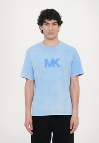 Gaiši zils kokvilnas T-krekls ar apaļu kakla izgriezumu, īsām piedurknēm un tumši zilu "MK" logotipu priekšpusē. Mīksta, nolietota tekstūra.