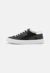 Sneaker in pelle sintetica nera lucida con motivo coccodrillo in rilievo; suola in gomma bianca, lacci e accentuazione del tallone; marchiato "Guess" di lato.