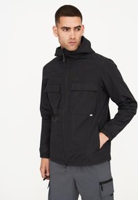 Schwarze leichte Jacke mit Kapuze, zwei großen Fronttaschen, elastischen Bündchen und Reißverschluss, aus wasserabweisendem Material gefertigt.