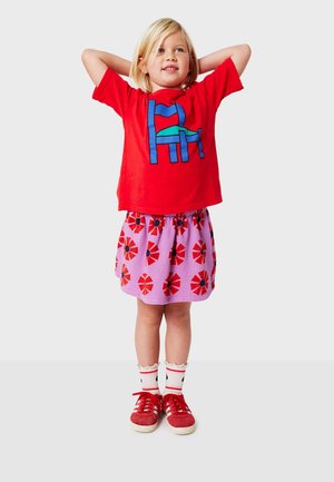Red cotton t-shirt with a blue and green graphic design, paired with a pink skirt featuring red flowers. Red sneakers with white socks.