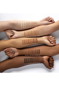 Échantillons de teintes de peau affichés sur plusieurs bras dans différentes nuances, allant du beige clair au brun foncé, étiquetés avec des numéros correspondants.