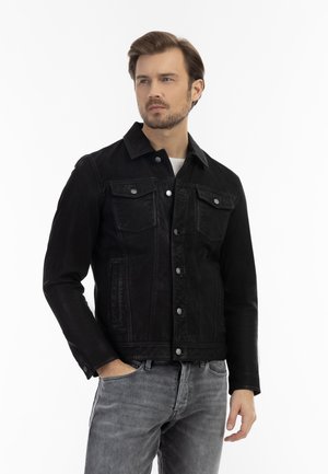 Jachetă din denim negru cu un design clasic, având buzunare frontale, nasturi metalici și un finisaj ușor texturat. Poartă o cămașă albă dedesubt.