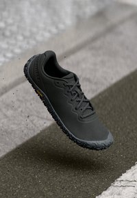 Svart sportig sko med texturerad sula och snören, hängande ovanför asfalt och övergångsställen.