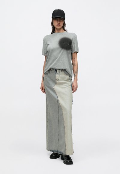 Naine, kes kannab halli T-särki musta rinnamustriga, kahetoonilist pika teksaseelikuga, musta platvormkingade ja musta pesapallimütsiga.