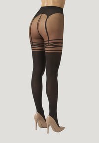 Persona che indossa collant neri trasparenti a motif e scarpe col tacco nudo, mostrata di spalle su uno sfondo chiaro e semplice.