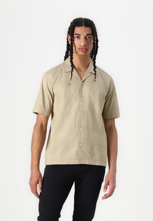 Short-sleeved beige shirt made of a textured fabric, featuring a pointed collar and button front, paired with black trousers.