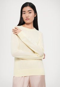 Helekollane kootud kampsun, millel on pikad soonikkoes varrukad, ümmargune kaelus ja pehme tekstuur, kombineeritud sujuvate roosade pükstega.