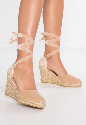 Escarpins compensés beige avec un talon tissé texturé, une tige en toile et des liens en ruban croisés à la cheville. Surface lisse avec des détails subtils.