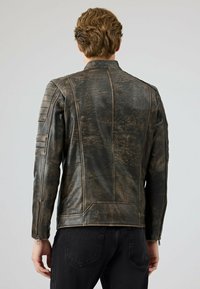 Bruine leren jas met een gestructureerd oppervlak, geribbelde schouderaccenten en ritsmanchetten. Strakke pasvorm en naden op het rugpand.