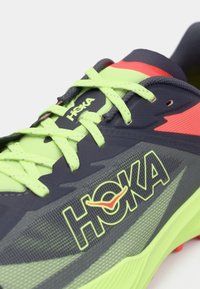 Ανδρικό αθλητικό παπούτσι σε ναυτικό μπλε με φωτεινές πράσινες λεπτομέρειες και λογότυπο. Διαθέτει υφασμάτινο επάνω μέρος με υφή και φωτεινές κοραλί λεπτομέρειες στη φτέρνα.