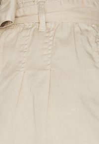 Beżowe spodnie z tkaniny z plisowanym wzorem, gładką fakturą, elastycznym pasem i widocznymi detalami przeszycia.