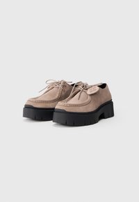 Chaussures plateformes en daim beige avec un bout arrondi, un design à lacets et une semelle en caoutchouc noir présentant des rainures profondes pour une meilleure adhérence.
