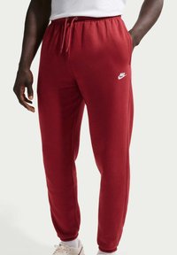 Pantalon de survêtement en coton rouge avec taille élastique et cordon de serrage. Présente le logo Nike blanc sur la cuisse gauche, des jambes fuselées et des poignets côtelés.