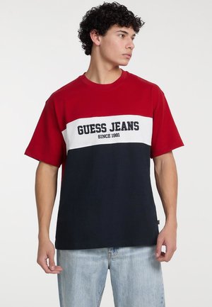 T-shirt w kolorze czerwonym, białym i granatowym, z blokowaniem kolorów, z napisem „GUESS JEANS” i detalem „SINCE 1981”, wykonany z miękkiej bawełny. Krótkie rękawy, luźny krój.