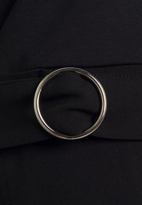 Czarna tkanina z sylwerowym okrągłym pierścieniem jako akcentem paska. Tekstura jest gładka z lekko błyszczącym wykończeniem.