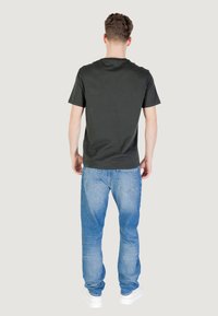 T-shirt in cotone nero a maniche corte, vista da dietro, abbinata a jeans in denim azzurri e sneaker bianche. Design semplice e casual.