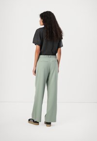 Light green wide-leg pants with a smooth texture, paired with a loose-fitting black t-shirt. The pants feature a gathered elastic waistband.