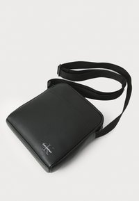 Sac en cuir synthétique noir en bandoulière avec une sangle ajustable, de forme rectangulaire, texture lisse et logo Calvin Klein subtil à l'avant.