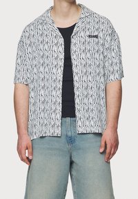 Camisa de manga corta en patrón ondulado blanco y negro; tela ligera; cuenta con un cuello en pico y un logo bordado en el pecho.