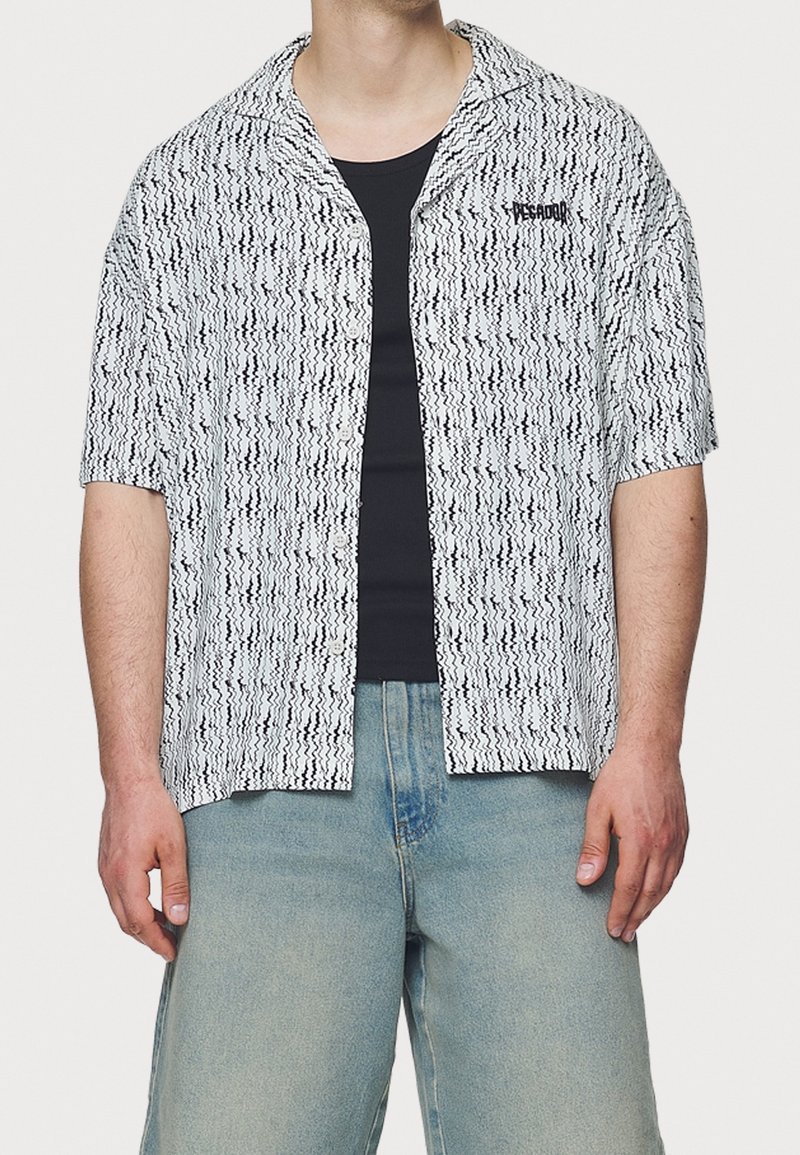 Camisa de manga corta en patrón ondulado blanco y negro; tela ligera; cuenta con un cuello en pico y un logo bordado en el pecho.
