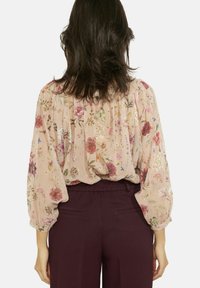 Ziedu blūze gaiši rozā krāsā ar garām, uzpūstām piedurknēm un atpakaļ savākta dizainā. Kopā ar tumši vīnsarkaniem biksēm.