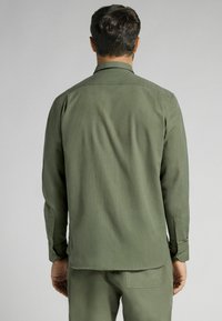Olijfgroene blouse met lange mouwen, een standaard kraag, knoopmanchetten en een rechte zoom. Glad textiel met een subtiele glans en minimale details.