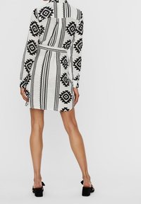 Svart och vit mönstrad klänning med krage, långa ärmar och insvängd midja. Har geometriska mönster och rak skärning.