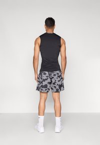 Αμάνικη μαύρη μπλούζα και γκρι σορτς με καμουφλάζ, που παρουσιάζουν υφή με μοτίβο. Λευκά αθλητικά παπούτσια και κάλτσες ολοκληρώνουν την αθλητική εμφάνιση από πίσω.