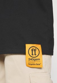 Sort bomuld t-shirt med korte ærmer, der har et orange syet mærke med brandlogoet og teksten "240gsm".