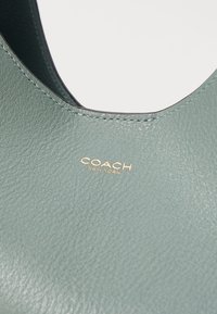 Green leather handbag featuring a smooth texture and subtle stitching. Includes a gold "COACH NEW YORK" logo. Designed with a rounded opening.