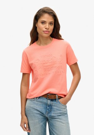 Coral cotton t-shirt with embossed "SuperDry" logo, crew neckline, and short sleeves, paired with light blue high-waisted jeans.