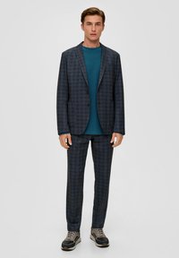 Tweedelig kostuum met een donker geruite blazer met twee knopen en brede revers, gecombineerd met bijpassende broek en een turquoise ronde hals T-shirt.