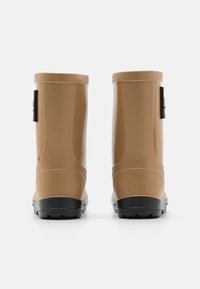Bottes de pluie en caoutchouc marron avec une finition brillante, présentant une semelle noire et une sangle latérale. Design haut, solides et imperméables.