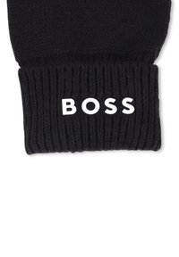 Črna pletena kapa z rebrasto teksturo in prepogibnim robom, na katerem je v beli barvi odločno prikazan napis "BOSS".
